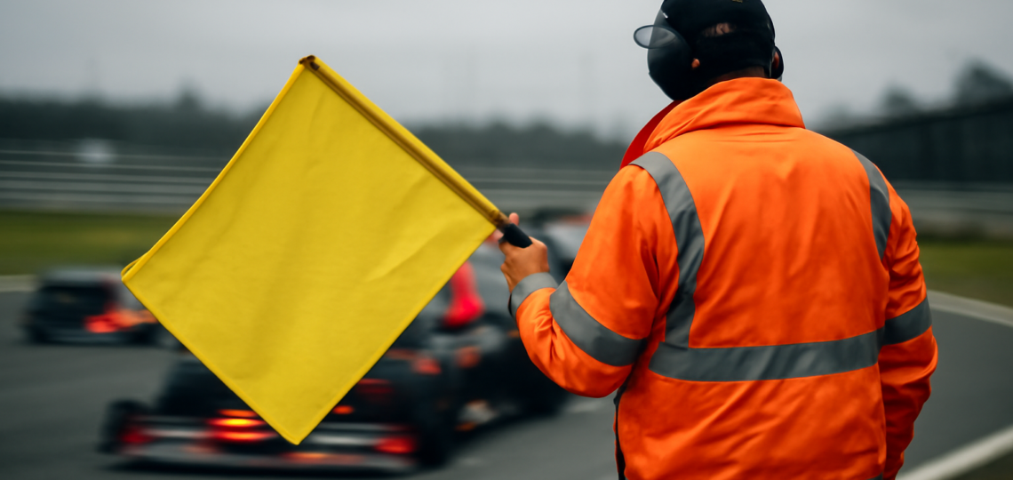 Marshal mengibarkan bendera kuning di tepi sirkuit Formula 1 saat mobil balap melintas